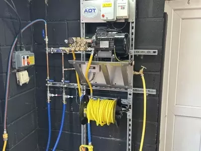 Custom wall-mounted pressure washer system with pump hardware and 20-metre hose reel installed in a vehicle detailer&rsquo;s workshop in Coalville.